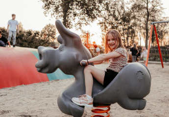 Bambina gioca su una molla a forma di animale in un parco giochi presso un alloggio glamping.