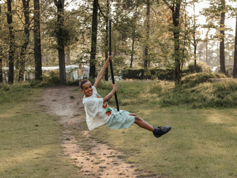 Niña sonríe columpiándose en una cuerda en el bosque, disfrutando del día en un alojamiento glamping.