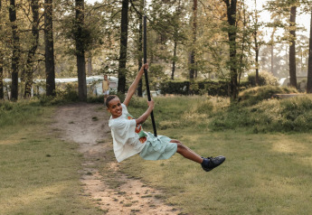 Niña sonríe columpiándose en una cuerda en el bosque, disfrutando del día en un alojamiento glamping.