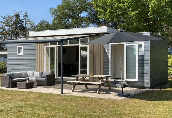 Chalet de lujo con fachada gris y madera, terraza con muebles de jardín, mesa de picnic y gran sombrilla.