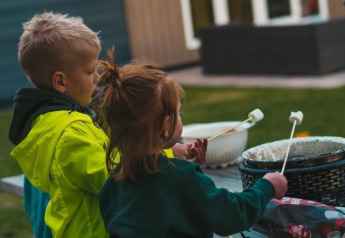 Twee kinderen roosteren marshmallows buiten aan het Luxury Chalet in Recreatiepark De Achterste Hoef, Nederland.