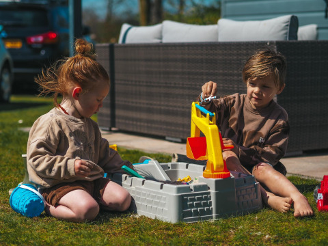 Twee kinderen spelen met een zandbak op het gras bij het Luxury Chalet in Recreatiepark De Achterste Hoef.
