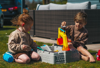 Dos niños juegan con un set de juguetes de arena en el césped del Luxury Chalet en Recreatiepark De Achterste Hoef.