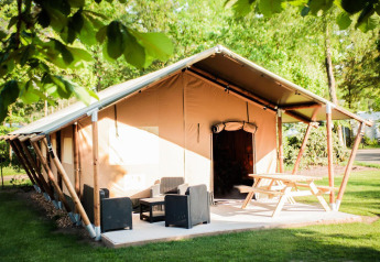 Safari tent with inviting patio, outdoor seating, and picnic table surrounded by lush green trees.