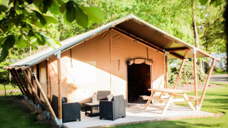 Tienda de safari con patio acogedor, muebles de exterior y mesa de picnic entre árboles verdes y sol.