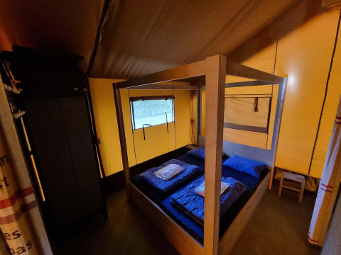 Vista interior de la Safaritent en Recreatiepark De Achterste Hoef con cama con dosel y ropa de cama azul.