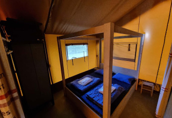 Vista interior de la Safaritent en Recreatiepark De Achterste Hoef con cama con dosel y ropa de cama azul.