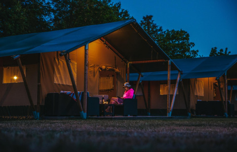 Aftenbillede af en person der sidder foran en safari-telt på Recreatiepark De Achterste Hoef, Nederlandene.