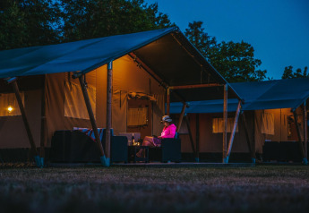 Foto serale di una persona seduta fuori da una tenda safari al Recreatiepark De Achterste Hoef, Paesi Bassi.