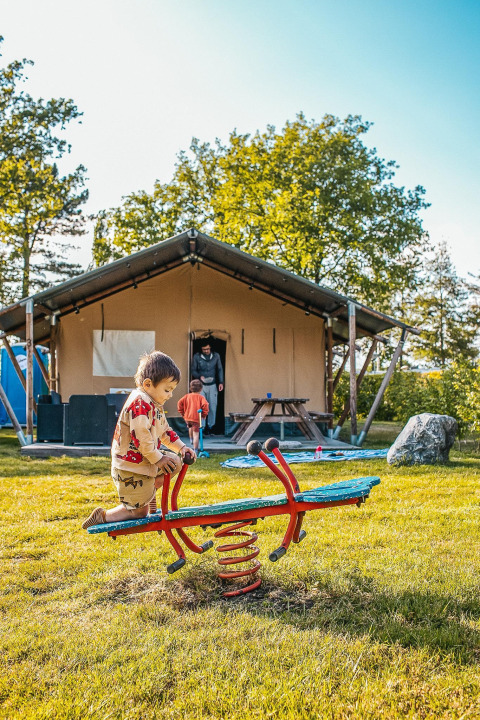 Kinderen spelen op een wip voor een safaritent bij Recreatiepark De Achterste Hoef in Nederland.