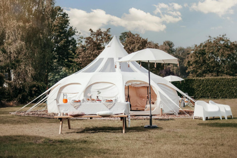 Una elegante tienda de safari Lotus Belle en un campo verde, con mesa para picnic y decoración blanca.