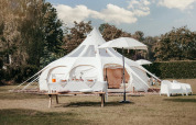 En luksuriøs Lotus Belle safari-telt på en grøn mark med et elegant udendørs opsætning og picnicbord.