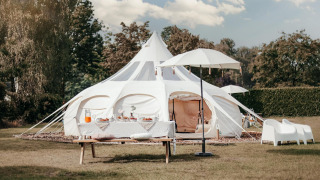 Een stijlvolle Lotus Belle safaritent op het gras, uitgerust met een picknicktafel en witte meubels.