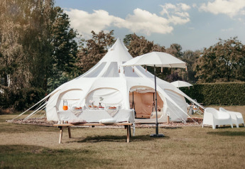 En luksuriøs Lotus Belle safari-telt på en grøn mark med et elegant udendørs opsætning og picnicbord.