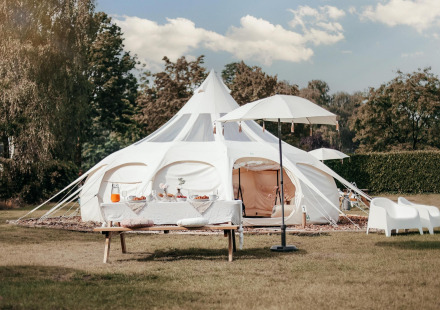 Een Lotus Belle safaritent op een grasveld, met stijlvol buitenterras en picknicktafel, wit ingericht.