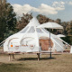 Una elegante tienda de safari Lotus Belle en un campo verde, con mesa para picnic y decoración blanca.