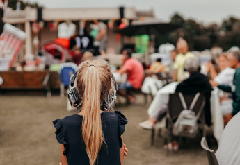 Een meisje met koptelefoon kijkt naar mensen aan tafels voor een tent op een recreatiepark in Nederland.