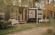 Cabañas modernas con grandes ventanales y asientos exteriores, rodeadas de árboles en un entorno natural.