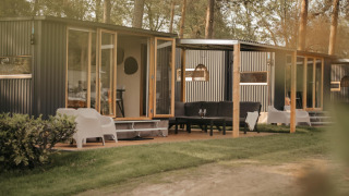 Cabañas modernas con grandes ventanales y asientos exteriores, rodeadas de árboles en un entorno natural.
