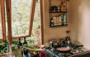 Accogliente cucina di cabina con finestra aperta, verdure fresche, vino e cottura sul fornello.