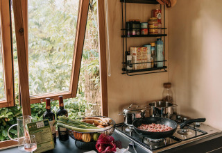 Acogedora cocina de cabaña con ventana abierta, verduras frescas, vino y cocina en la estufa.