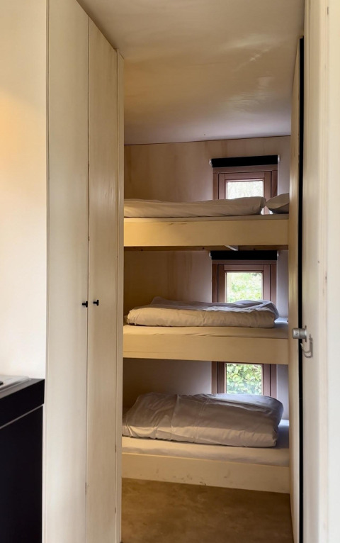 Foto van een cabine met drie stapelbedden, telkens voor een raam geplaatst, eenvoudige inrichting.