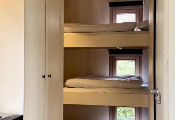 Foto di una stanza di cabina con tre letti a castello sovrapposti davanti alle finestre, arredamento semplice.