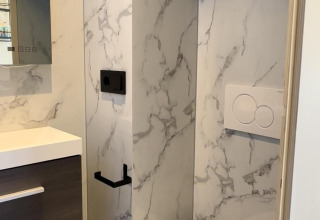 Moderne badeværelse i en hytte med væghængt toilet, marmorvæg og minimalistisk interiørdesign.