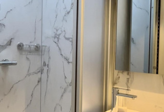 Baño moderno de cabina con paredes tipo mármol, ducha, lavabo y espejo, iluminado por luz natural.