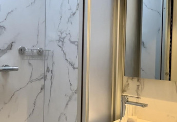 Salle de bain de cabine moderne avec murs effet marbre, douche, lavabo et miroir sous lumière naturelle.