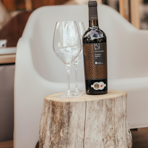 Botella de vino y dos copas sobre un tronco de árbol frente a un sillón en una cabaña acogedora.