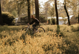 Eine Person fährt Fahrrad im grünen Wald bei Wohnwagen im Klapkot, Recreatiepark De Achterste Hoef, Niederlande.