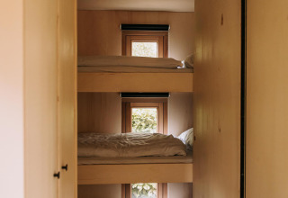 Literas triples con ropa de cama blanca en una cabaña de madera en Klapkot, De Achterste Hoef, Países Bajos.
