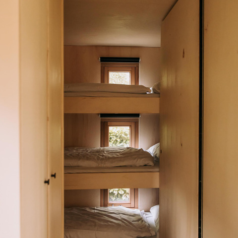 Triple bunk beds with white bedding in a wooden cabin at Klapkot, De Achterste Hoef, Netherlands.