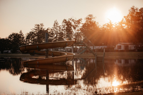 Solnedgang over en sø med rutsjebane ved Klapkot-hytten i Recreatiepark De Achterste Hoef, Holland.