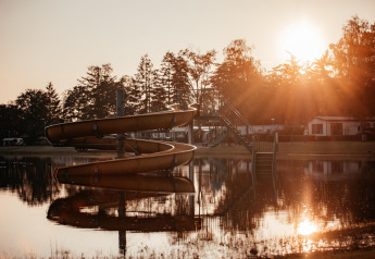 Solnedgang over en sø med rutsjebane ved Klapkot-hytten i Recreatiepark De Achterste Hoef, Holland.