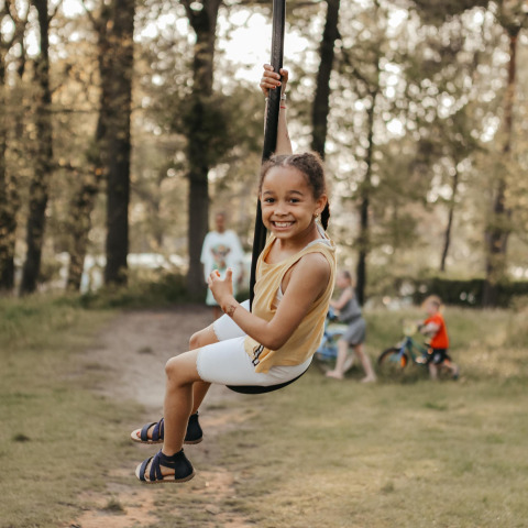 Un niño sonriente se lanza en tirolina en Waterlodge, Recreatiepark De Achterste Hoef, Países Bajos, entre árboles.