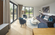 Moderne opholdsstue i Zypendaal Comfort-lodgen ved Veluwepark de Bosgraaf i Holland, med store vinduer.
