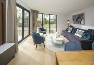 Sala moderna en la cabaña Zypendaal Comfort del Veluwepark de Bosgraaf en los Países Bajos, con grandes ventanales.