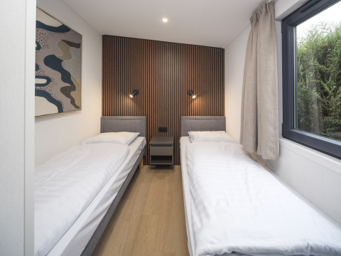 Habitación doble moderna con dos camas individuales, pared de madera, ventana grande y decoración minimalista.