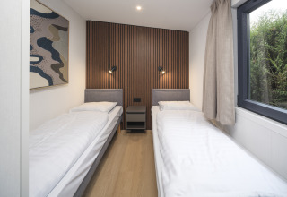 Habitación doble moderna con dos camas individuales, pared de madera, ventana grande y decoración minimalista.