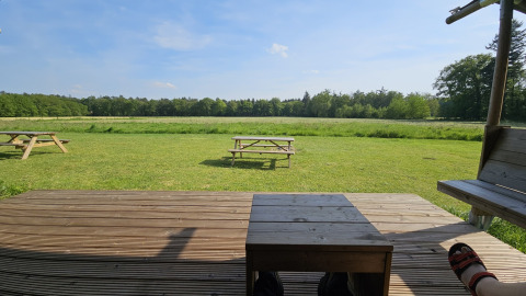 Blick von einer Holzterrasse auf grüne Wiesen und Bänke im Mooirust Ferienpark, Utrecht, Niederlande.