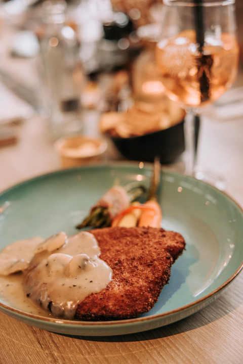 Escalope empanado con salsa de champiñones y verduras, servido en un plato azul en De Achterste Hoef.