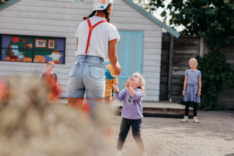 Kinder spielen draußen mit einem Erwachsenen bei einem Ferienhaus im Recreatiepark De Achterste Hoef.