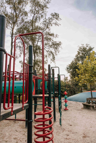 Speeltuin met klimrek en glijbaan in het zand, omgeven door bomen bij De Achterste Hoef, Nederland.