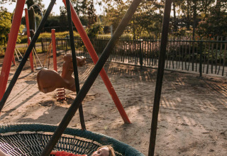 Barn med sut slapper af på en rund gynge i en legeplads på Recreatiepark De Achterste Hoef, Holland.