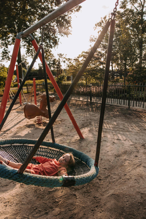 Enfant avec tétine allongé sur une balançoire ronde au terrain de jeu à De Achterste Hoef, Pays-Bas.