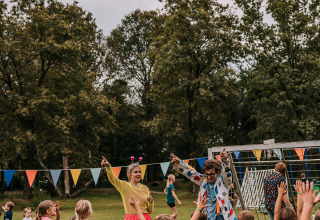 Kinder spielen draußen mit Erwachsenen in bunter Kleidung während einer Feier im Noord-Brabant, Niederlande.