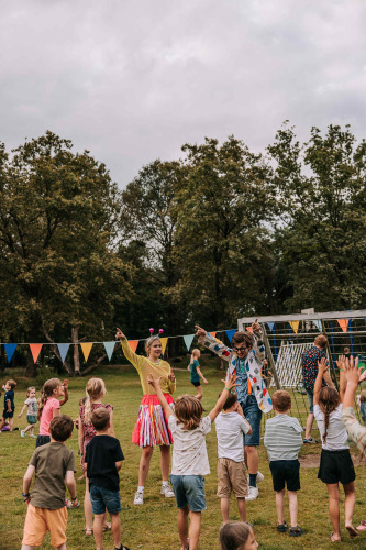 Kinderen spelen buiten met volwassenen in kleurrijke outfits tijdens een feest in een park in Noord-Brabant, Nederland.