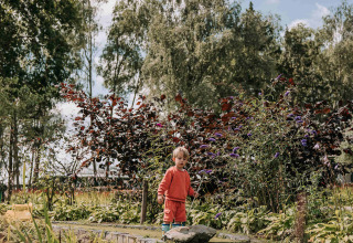 Een kind in oranje kledij bij een vijver met planten in Recreatiepark De Achterste Hoef, Noord-Brabant.